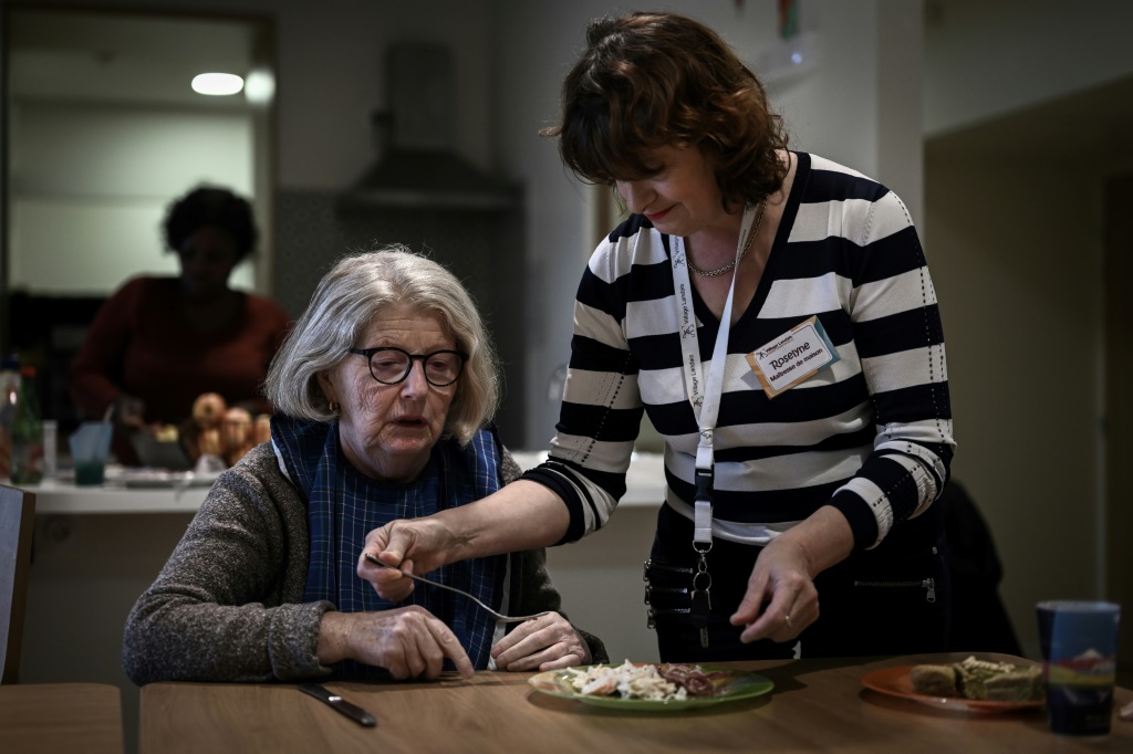 أحد العاملين في مجال الرعاية الصحية (على اليمين) يميل إلى مساعدة مريض مصاب بمرض الزهايمر على تناول وجبة الغداء (ا ف ب)