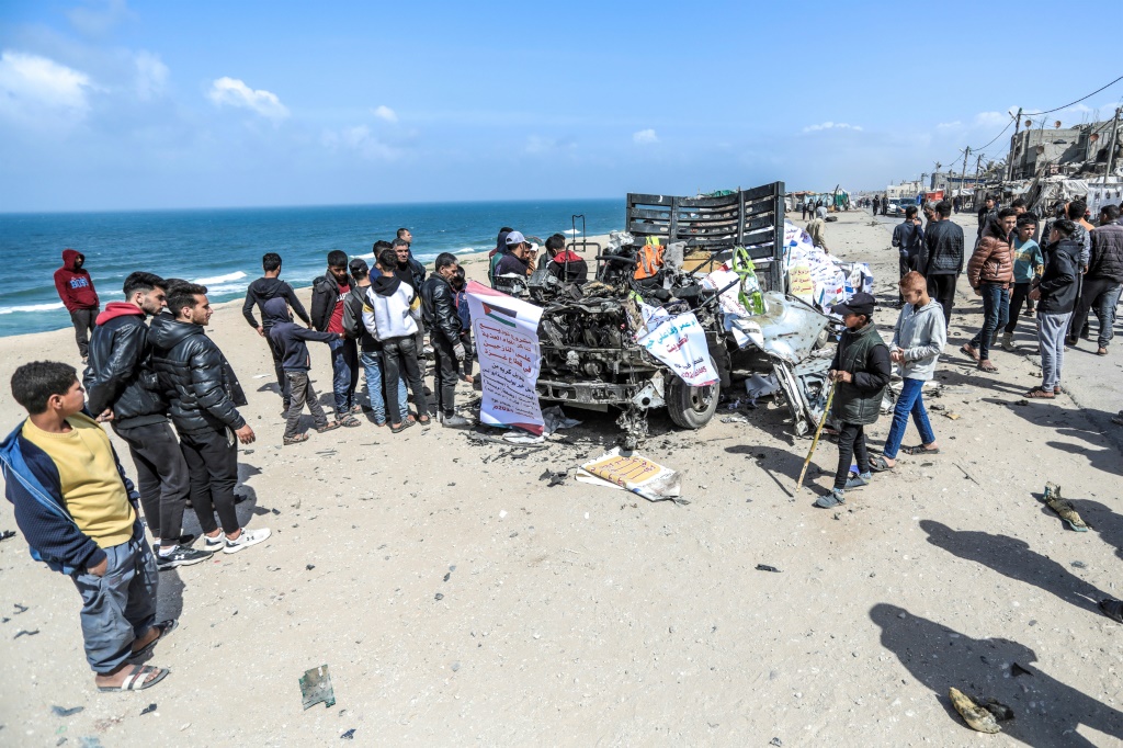 أشخاص يتجمعون حول شاحنة تحمل مساعدات إنسانية أفادت تقارير بأنها أصيبت في غارة جوية إسرائيلية على الطريق الساحلي الرئيسي في دير البلح وسط غزة في 3 آذار مارس 2024 (ا ف ب)