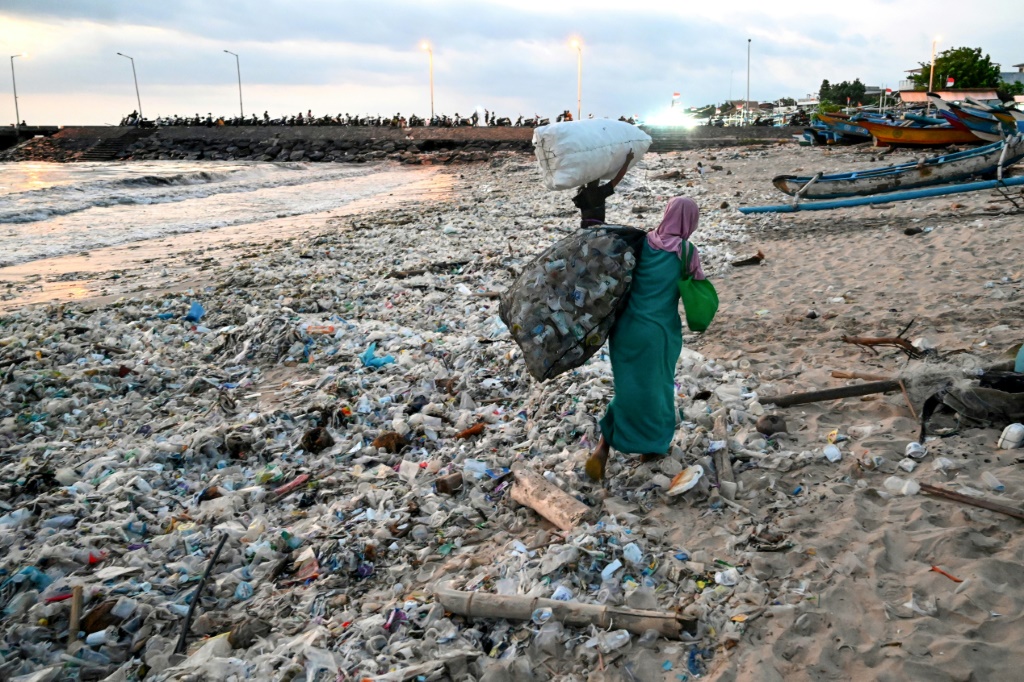 صورة التقطت في 19 آذار/مارس 2024 لامرأة تحمل كيساً من االنفايات القابلة لإعادة التدوير جرفتها الأمواج إلى شاطئ كيدونغانان في جزيرة بالي الإندونيسية (ا ف ب)