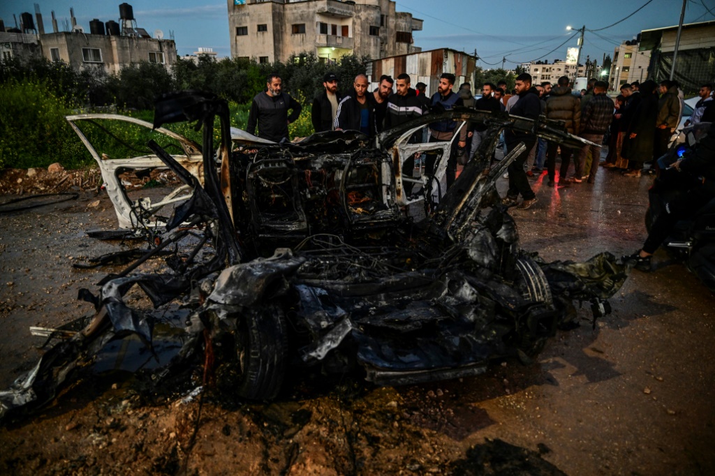 رجال فلسطينيون يحيطون بسيارة متفحمة أصيبت في غارة جوية إسرائيلية على جنين (أ ف ب)   
