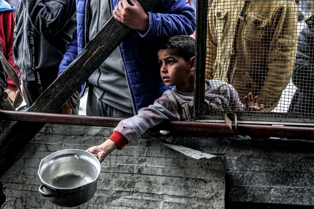 طفل يحاول الحصول على وجبة مع نازحين فلسطينيين آخرين من منظمة خيرية قبل الإفطار في رفح في حنوب قطاع غزة في 16 آذار مارس 2024 (ا ف ب)