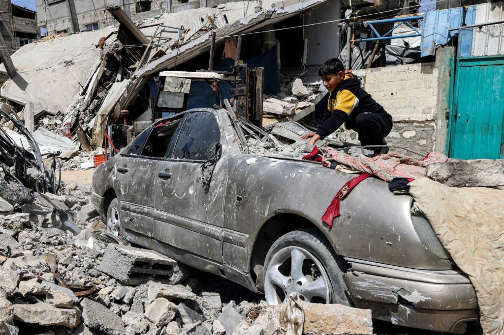 طفل يزيل ركاما عن سطح سيارة أًصيبت في القصف في رفح في جنوب قطاع غزة في الخامس من نيسان/أبريل 2024 (ا ف ب)