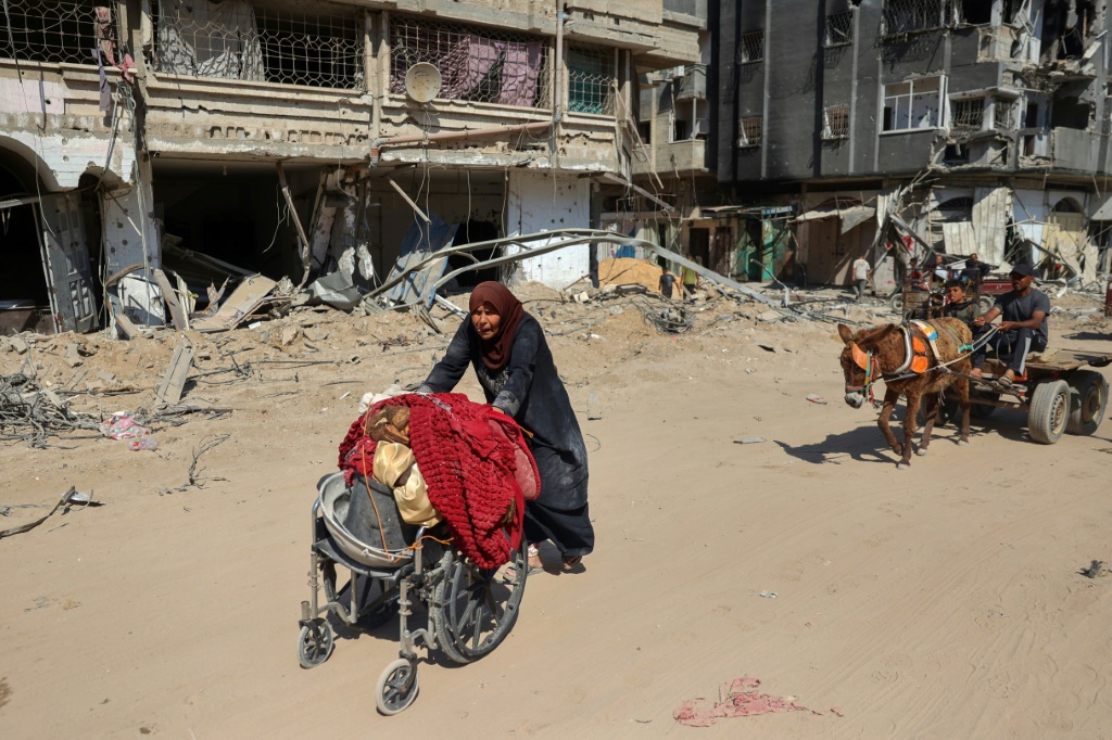  امرأة فلسطينية مسنة تستخدم كرسيا متحركا لنقل أمتعتها عبر المباني المتضررة في خان يونس في 7 نيسان/أبريل 2024 بعد أن سحبت إسرائيل قواتها من المدينة الواقعة في جنوب قطاع غزة (ا ف ب)