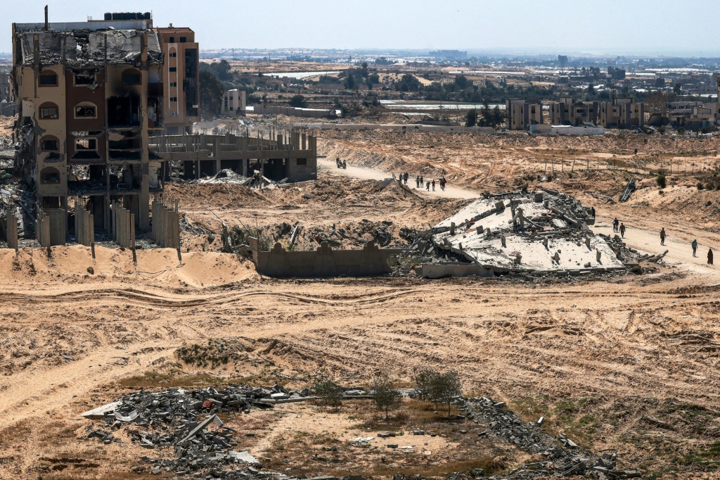 فلسطينيون يسيرون أمام المباني المتضررة والمدمرة في خان يونس في 7 نيسان أبريل 2024 بعد أن سحبت إسرائيل قواتها البرية من المدينة الواقعة غي جنوب قطاع غزة (ا ف ب)