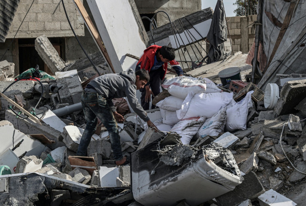 صبية فلسطينيون ينتشلون أكياس الطحين من بين أنقاض منزل دمره القصف الإسرائيلي في شمال رفح بجنوب قطاع غزة في 23 آذار مارس 2024 (ا ف ب)