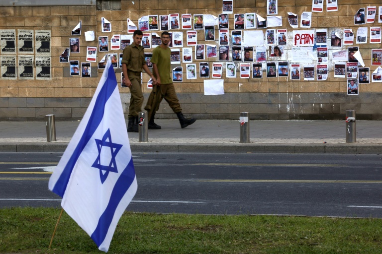 جنيدان يمران في 16 تشرين الأول/أكتوبر 2023 أمام حائط مبنى وزارة الدفاع الإسرائيلية في تل أبيب، حيث وُضعت صور لإسرائيليين اختطفتهم حركة حماس خلال هجومها على إسرائيل في السابع من الشهر عينه (أ ف ب)