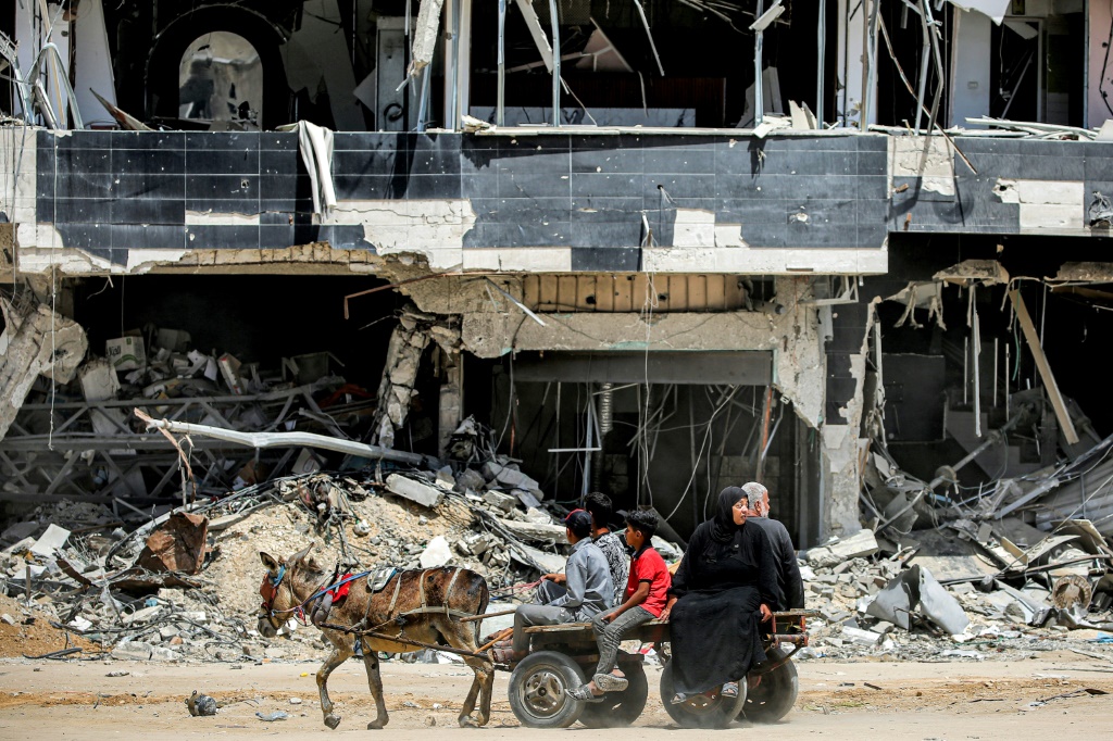 سكان غزة يركبون عربة يجرها حمار أمام مبنى مدمر في خان يونس (ا ف ب)
