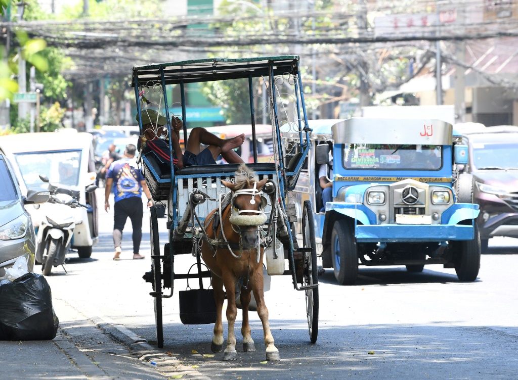 سائق عربة تجرّها خيول يحتمي تحت شجرة بينما ينتظر السياح على طول طريق في مانيلا في 24 نيسان/أبريل 2024 (ا ف ب)