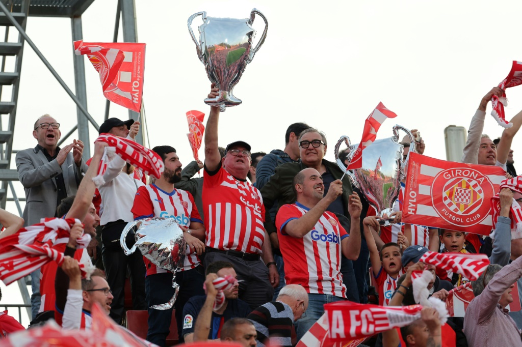 مشجعو جيرونا يلوّحون بالأعلام ويحمل أحدهم مجسّماً لكأس دوري أبطال أوروبا في مباراة فريقهم أمام برشلونة ضمن الدوري الإسباني لكرة القدم. 4 أيار/مايو 2024، ملعب مونتيليفي في جيرونا (ا ف ب)