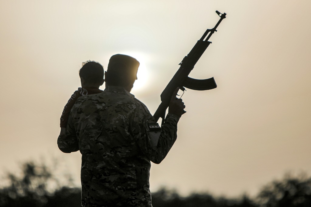 أحمد مقاتل سوري موال لتركيا يستخدم اسما مستعارا يحمل نجله وهما يمشيان في حقل في موقع في محافظة حلب في شمال سوريا في 26 نيسان/أبريل 2024 (ا ف ب)