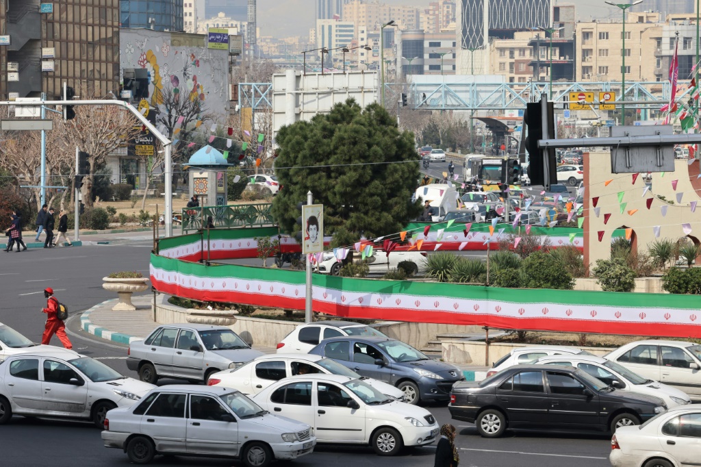  سيارات تمر بجوار جدار مغطى بألوان العلم الوطني الإيراني في طهران في 3 آذار/مارس 2024 (ا ف ب)