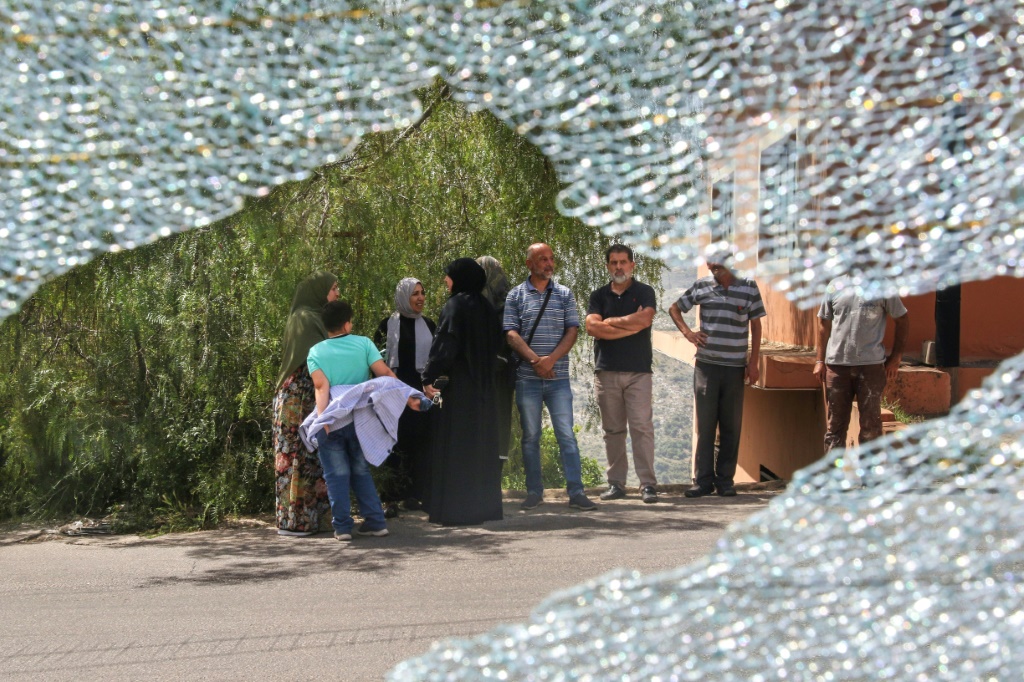 أشخاص يقفون على اطراف الطريق أمام حافلة متضررة جراء غارة اسرائيلية على طريق عام في منطقة النبطية في جنوب لبنان في 23 أيار/مايو 2024 (أ ف ب)   