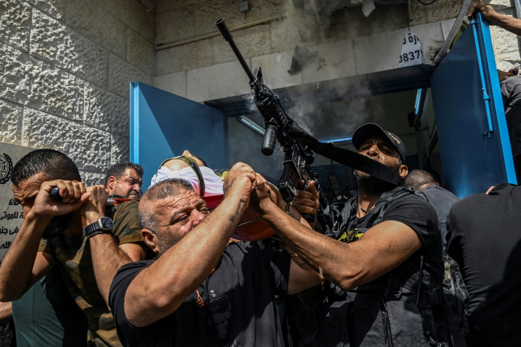 وكانت العديد من الجثث ملفوفة بالأعلام وسار بها حشود من الفلسطينيين، بما في ذلك مسلحون، في الشوارع (أ ف ب)   