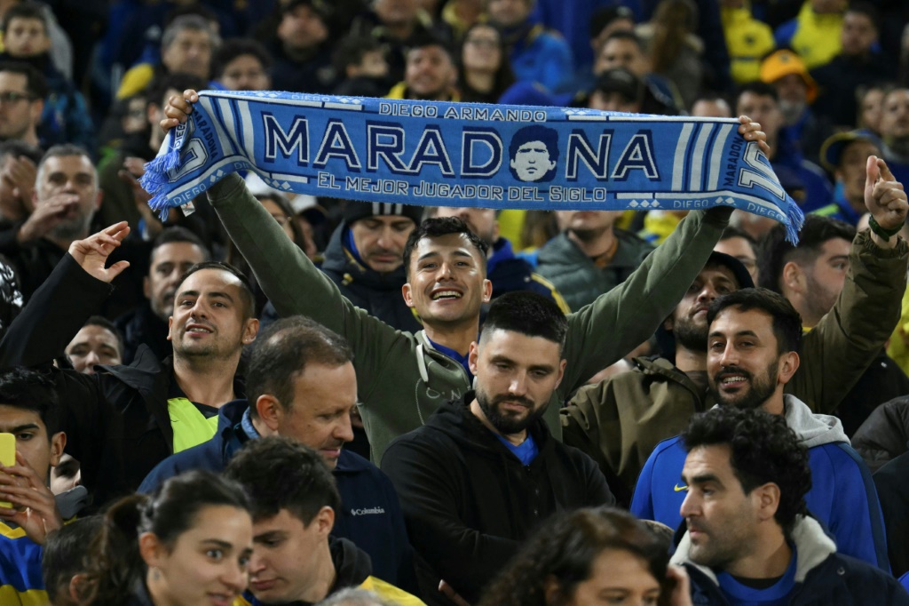 أحد مشجعي نادي بوكا جونيورز الأرجنتيني يحمل وشاحا تكريما للنجم دييغو مارادونا خلال مباراة فريقه في مسابقة كوبا سود أميركانا على ملعب لا بومبونيرا في بوينس آيرس في 15 أيار/مايو 2024 (ا ف ب)