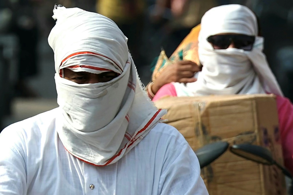 يقوم الأشخاص الذين يركبون الدراجات بتغطية وجوههم بقطعة قماش بعد ظهر أحد أيام الصيف الحارة في فاراناسي يوم 29 مايو (أ ف ب)   