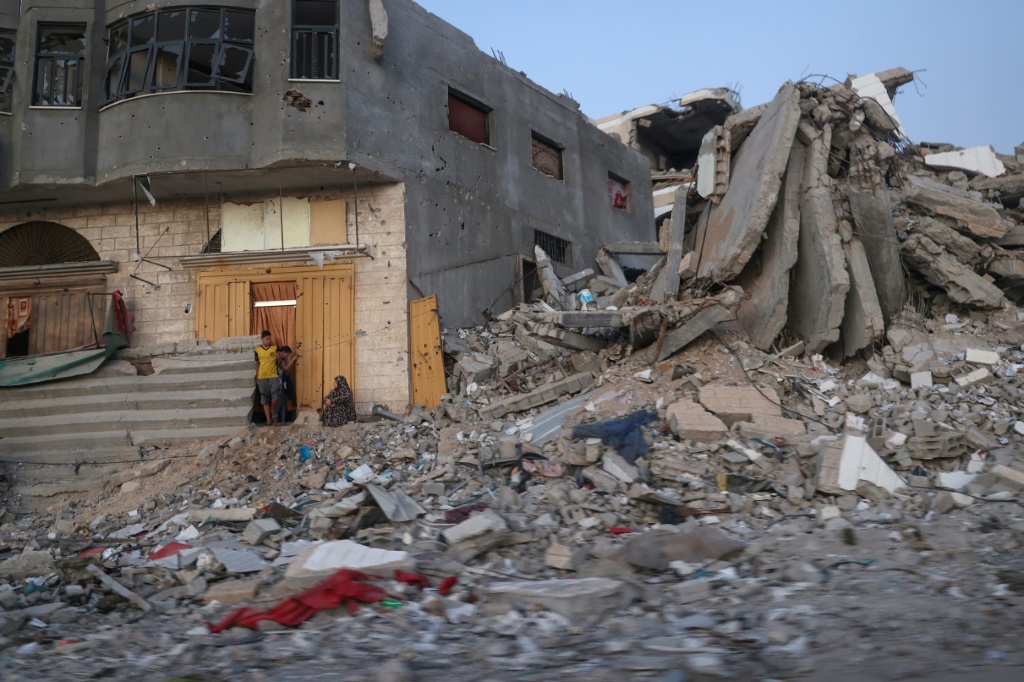 فلسطينيون يجلسون بجوار مبنى مدمر محاط بالأنقاض في مخيم البريج وسط قطاع غزة يوم الأحد (ا ف ب)