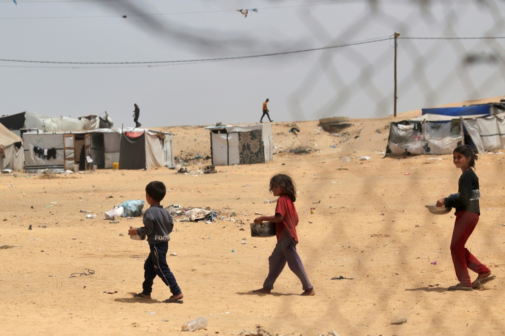 أطفال فلسطينيون نازحون يحملون حاويات طعام في رفح، 19 مايو، 2024، وسط الصراع المستمر بين إسرائيل وحماس. (أ ف ب)   