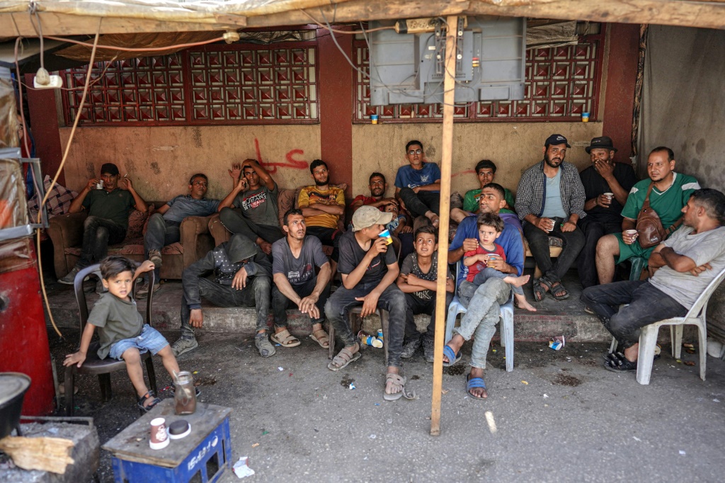 رجال وفتيان فلسطينيون يجلسون لمشاهدة تلفزيون مشترك في دير البلح وسط قطاع غزة في 7 حزيران/يونيو 2024 (أ ف ب)   
