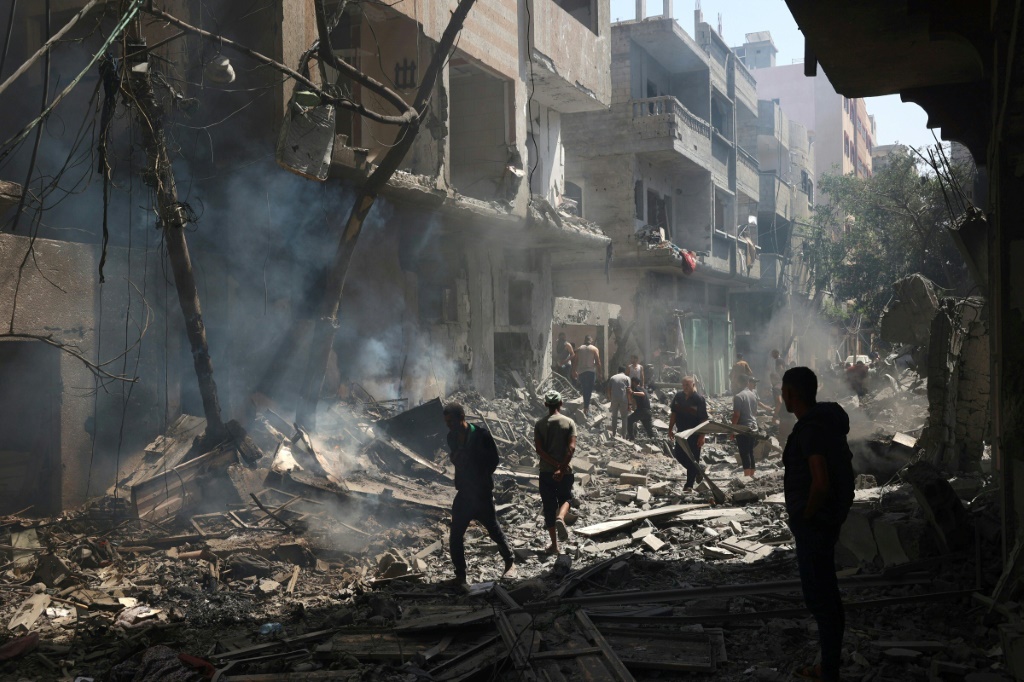 فلسطينيون يسيرون في الثامن من حزيران/يونيو 2024 وسط انقاض أبنية دمرت خلال العدوان الإسرائيلي لتخليص رهائن في مخيم النصيرات في وسط قطاع غزة (أ ف ب)