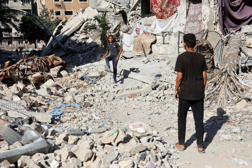 أطفال فلسطينيون يلعبون كرة القدم محاطين بأنقاض المباني التي دمّرت خلال القصف الإسرائيلي غلى مدينة غزة في العاشر من حزيران/يونيو 2024 (أ ف ب)   