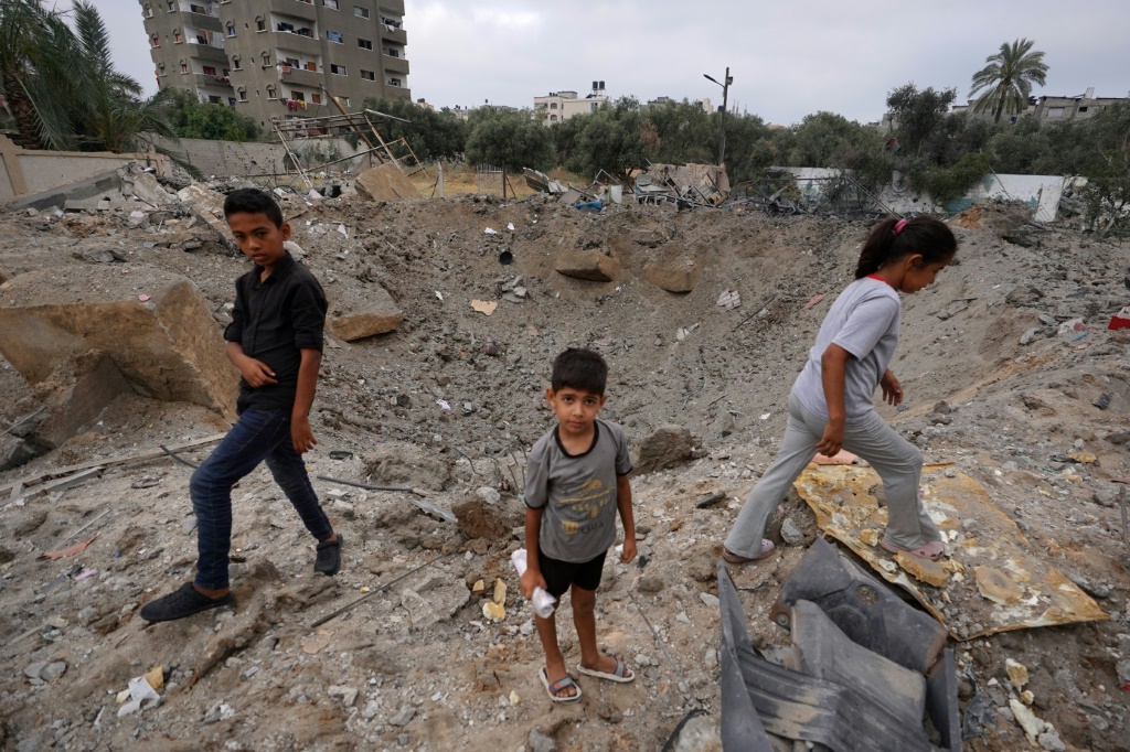 أطفال فلسطينيون بالقرب من الحفرة التي خلفتها غارة إسرائيلية في النصيرات وسط قطاع غزة في 3 يونيو 2024 (أ ف ب)