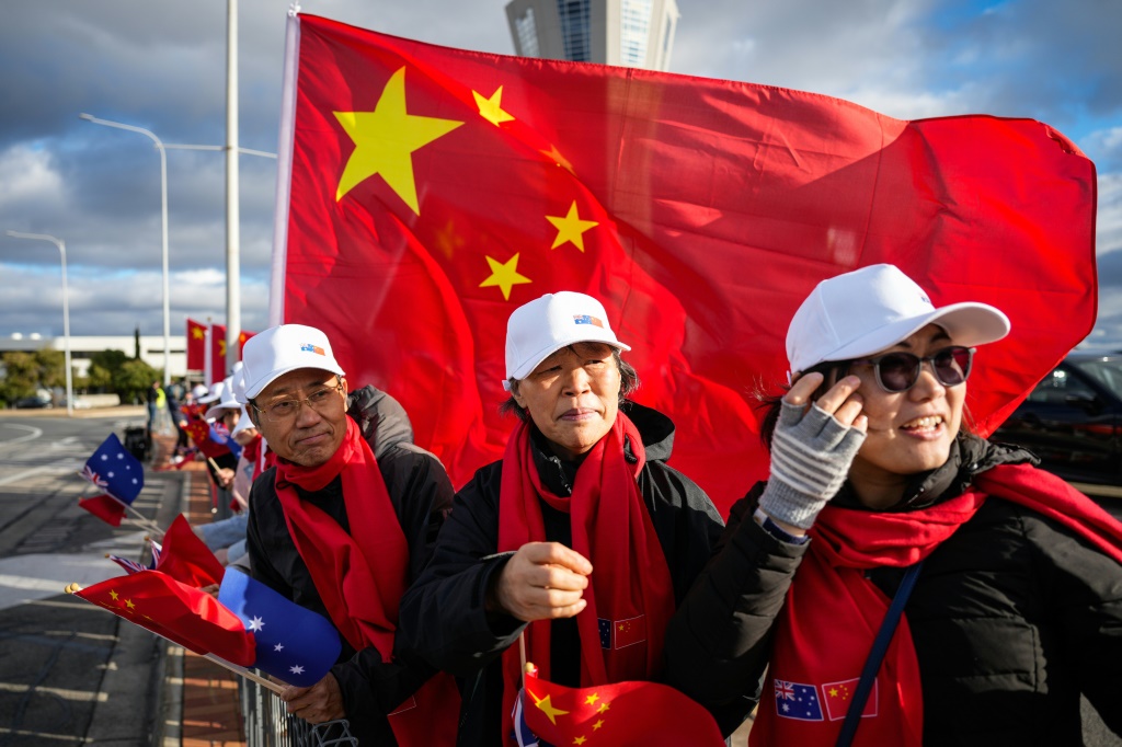 أشخاص يلوحون بالأعلام الوطنية الصينية وهم ينتظرون وصول رئيس مجلس الدولة الصيني لي تشيانغ إلى أديلايد في 15 حزيران/يونيو 2024 (ا ف ب)