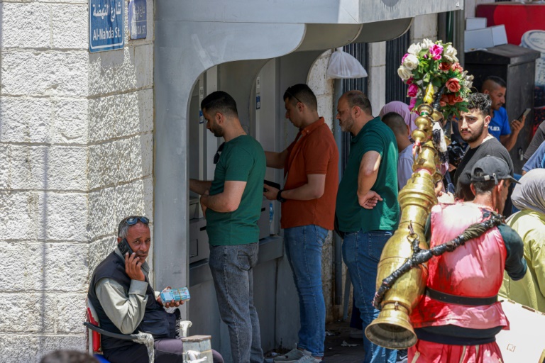 فلسطينيون ينتظرون أمام صرّاف آلي لسحب أموال في سوق رام الله بالضفة الغربية المحتلة في 9 حزيران/يونيو 2024 (ا ف ب)