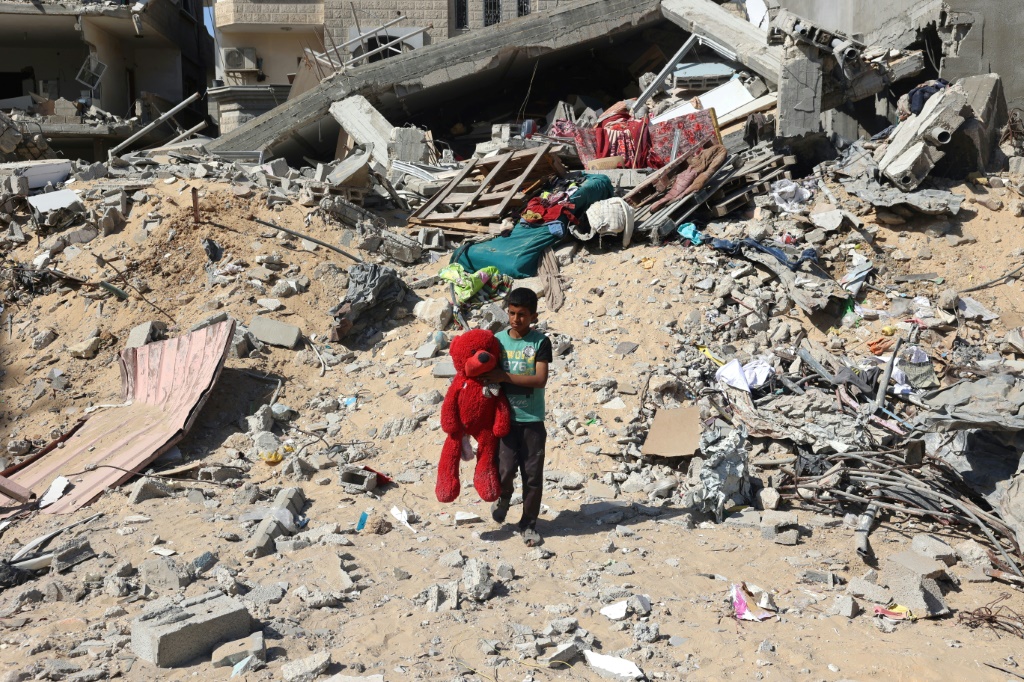 طفل فلسطيني يحمل دمية عثر عليها بين انقاض مبنى دمر في قصف إسرائيلي في خان يونس في 21 حزيران/يونيو 2024 (أ ف ب)   