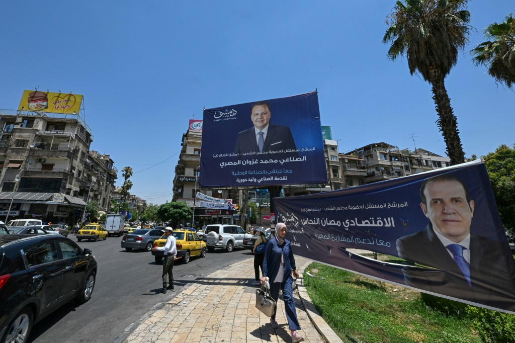    مارة وسط شارع في دمشق في 10 تموز/يوليو 2024 قرب صور لمرشحين للانتخابات التشريعية وهي الرابعة منذ اندلاع النزاع الذي يعصف بالبلاد منذ أكثر من 13 عاماً (أ ف ب)   