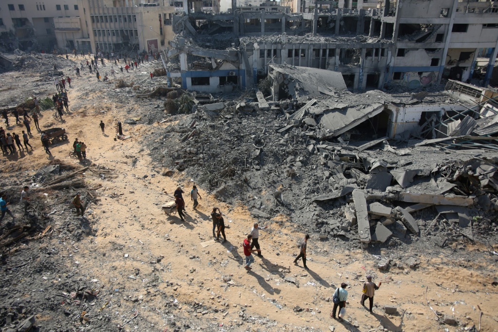 مدنيون فلسطينيون يسيرون أمام أنقاض المباني التي تعرضت للقصف في حي الصناعة بمدينة غزة بعد قصف القوات الإسرائيلية. (أ ف ب)   