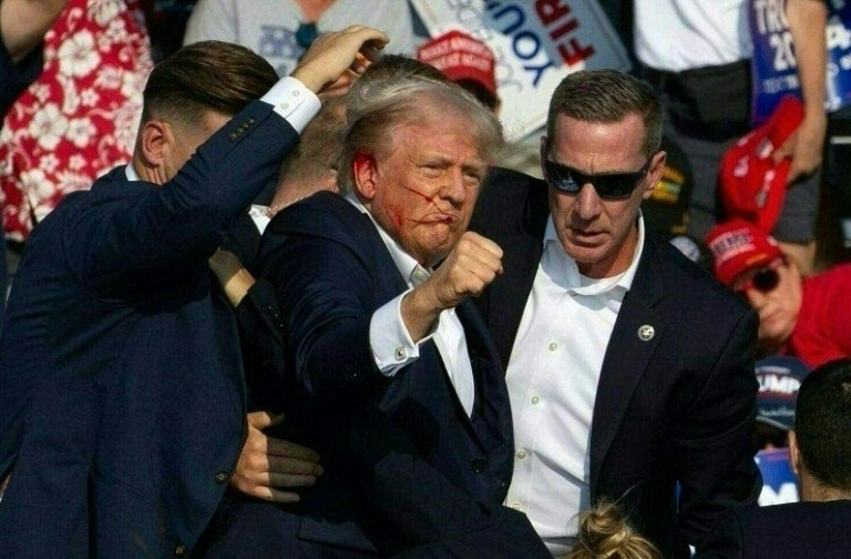 المرشح الجمهوري دونالد ترامب وما يبدو أنه دماء على وجهه محاطًا بعملاء الخدمة السرية أثناء إنزاله من المسرح في . في بتلر، بنسلفانيا، 13 يوليو  2024(أ ف ب) 