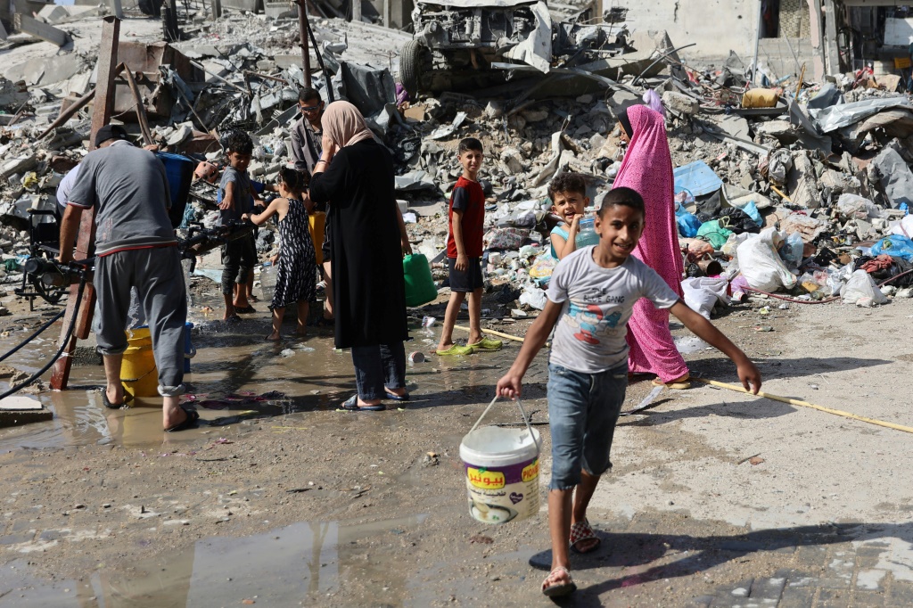 طفل فلسطيني يحمل دلو ماء مملوء من أنبوب في مخيم جباليا للاجئين في شمال قطاع غزة في 20 حزيران/يونيو 2024 (أ ف ب)   