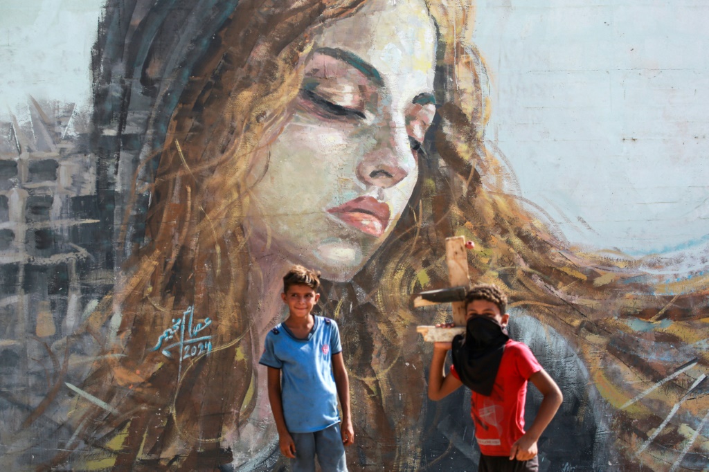 فتية أمام جدارية للفنان الفلسطيني عصام مخيمر (33 عامًا) النازح من مدينة غزة، على جدار في مخيم مؤقت للنازحين في دير البلح وسط قطاع غزة في 26 تموز/يوليو 2024 (أ ف ب)   
