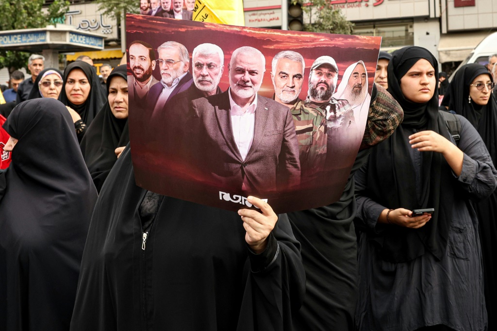    امرأة إيرانية تحمل ملصقًا يظهر قادة مسلحين مقتولين بما في ذلك زعيم حماس إسماعيل هنية أثناء موكب جنازته في طهران (أ ف ب)   