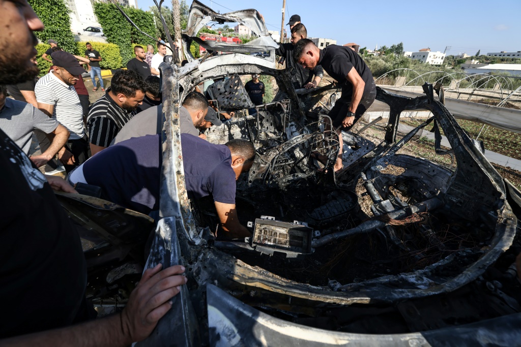 صورة مؤرخة في 3 آب/أغسطس 2024 لأشخاص قرب سيارة استُهدفت بقصف إسرائيلي في طولكرم في الضفة الغربية المحتلة (أ ف ب)   