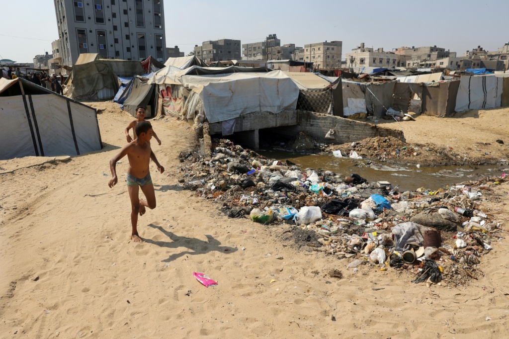 أطفال يلعبون بجوار القمامة ومياه الصرف الصحي في مخيم للنازحين الفلسطينيين في دير البلح وسط قطاع غزة (أ ف ب)   