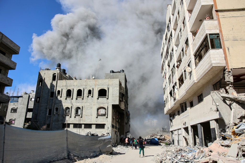 فلسطينيون في مدينة غزة يشاهدون تصاعد الدخان من مبنى تعرض لقصف بعد تحذير الجيش الإسرائيلي لسكانه بإخلائه (أ ف ب)   