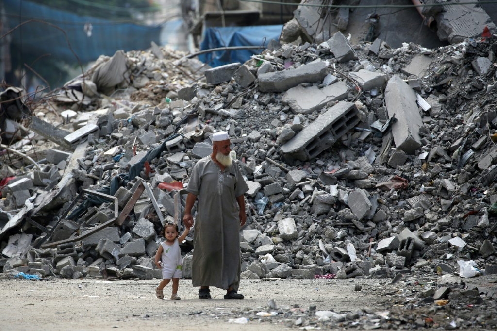 فلسطينيون يسيرون أمام أنقاض مخيم البريج للاجئين في وسط غزة بعد أكثر من عشرة أشهر من بدء الحرب بين إسرائيل وحماس (أ ف ب)   