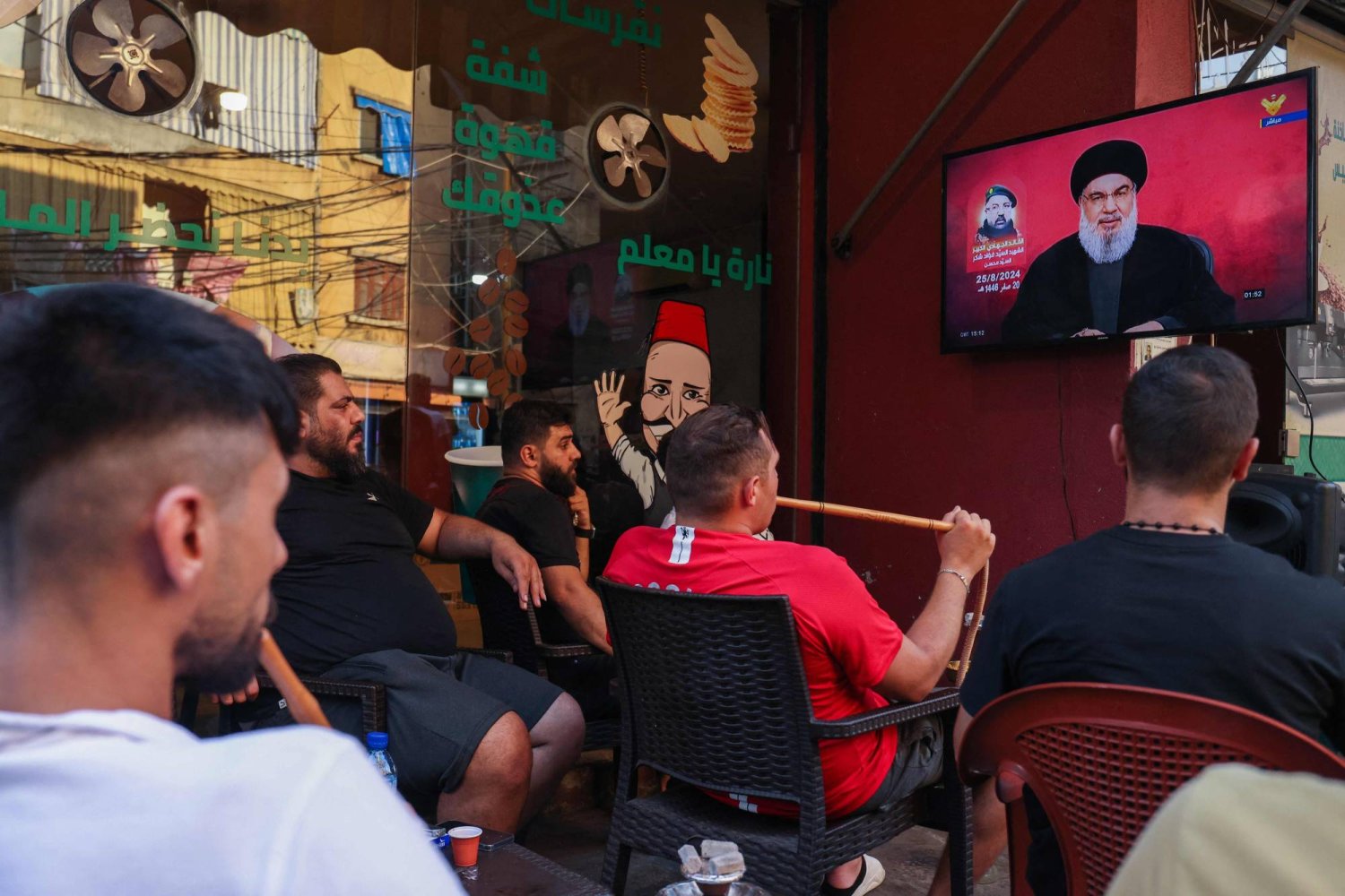 شبان لبنانيون يستمعون في مقهى بمنطقة الشياح في ضاحية بيروت الجنوبية إلى كلمة أمين عام «حزب الله» حسن نصر الله متحدثا عن الردّ على اغتيال القيادي فؤاد شكر (أ.ف.ب)