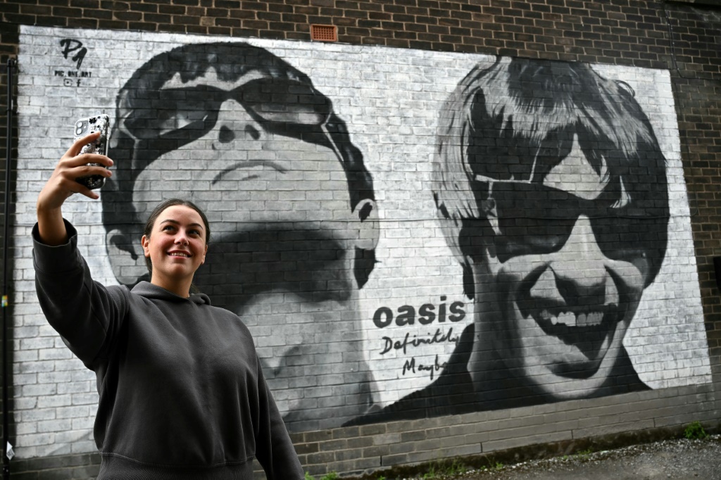 يحتفل محبو فرقة Oasis بعودة الفرقة، حيث يقفون أمام جدارية من إبداع فنان الشارع Pic.One.Art المقيم في مانشستر على جانب ألبوم Sifters Record (أ ف ب)   