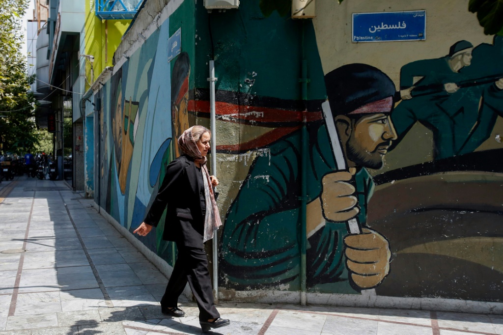امرأة تمر أمام لوحة جدارية تصور أعضاء من الحرس الثوري الإيراني في ساحة فلسطين بطهران في الثامن من آب/أغسطس 2024 (أ ف ب)