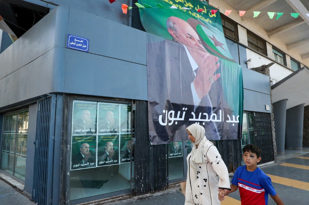 أشخاص يمرّون قرب دعاية انتخابية للرئيس الجزائري عبد المجيد تبون في وهران في الخامس من ايلول/سبتمبر 2024 (أ ف ب)   