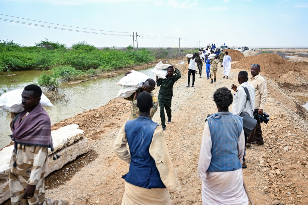 رجال وجنود من الجيش السوداني يحملون أكياسا من الإمدادات الغذائية لمساعدة الأشخاص العالقين في منطقة غمرتها المياه في طوكر في ولاية البحر الأحمر، في أعقاب الفيضانات الغزيرة الأخيرة في شرق السودان، في الخامس من أيلول/سبتمبر 2024 (أ ف ب)   