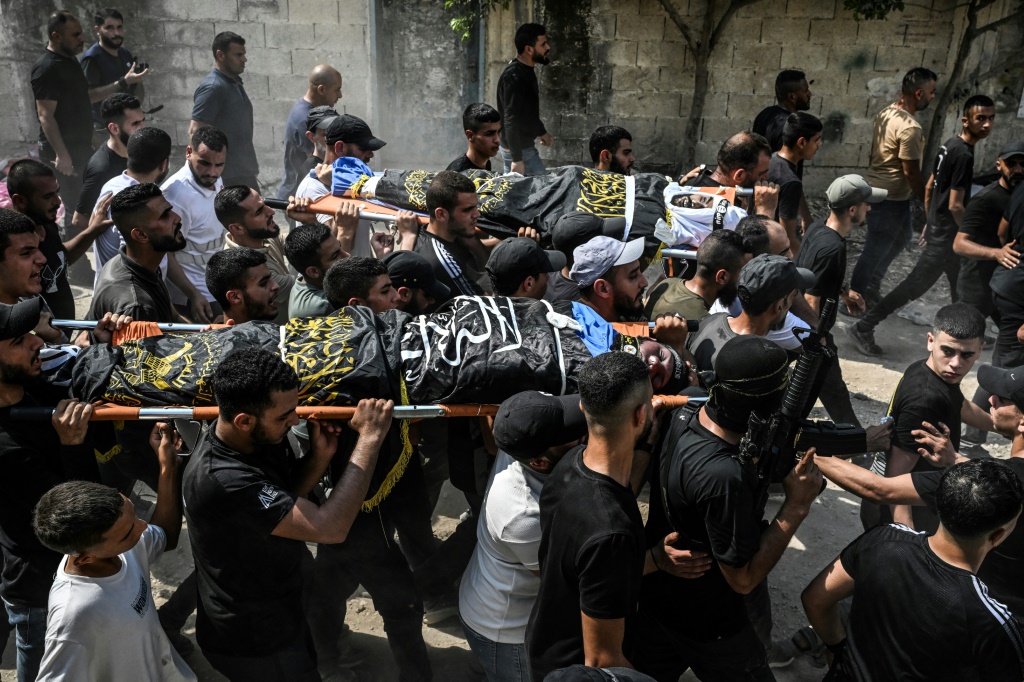 مشيعون في مخيم جنين للاجئين يحملون جثث الفلسطينيين الذين قتلوا خلال الغارة الإسرائيلية (أ ف ب)   
