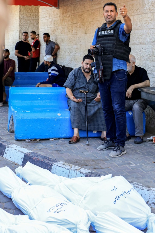 المصور الصحافي في وكالة فرانس برس محمود الهمص يحمل كاميرته قرب جثامين ضحايا قصف إسرائيلي قبل مواراتهم الثرى في دير البلح وسط قطاع غزة في 31 تشرين الأول/أكتوبر 2023 (أ ف ب)