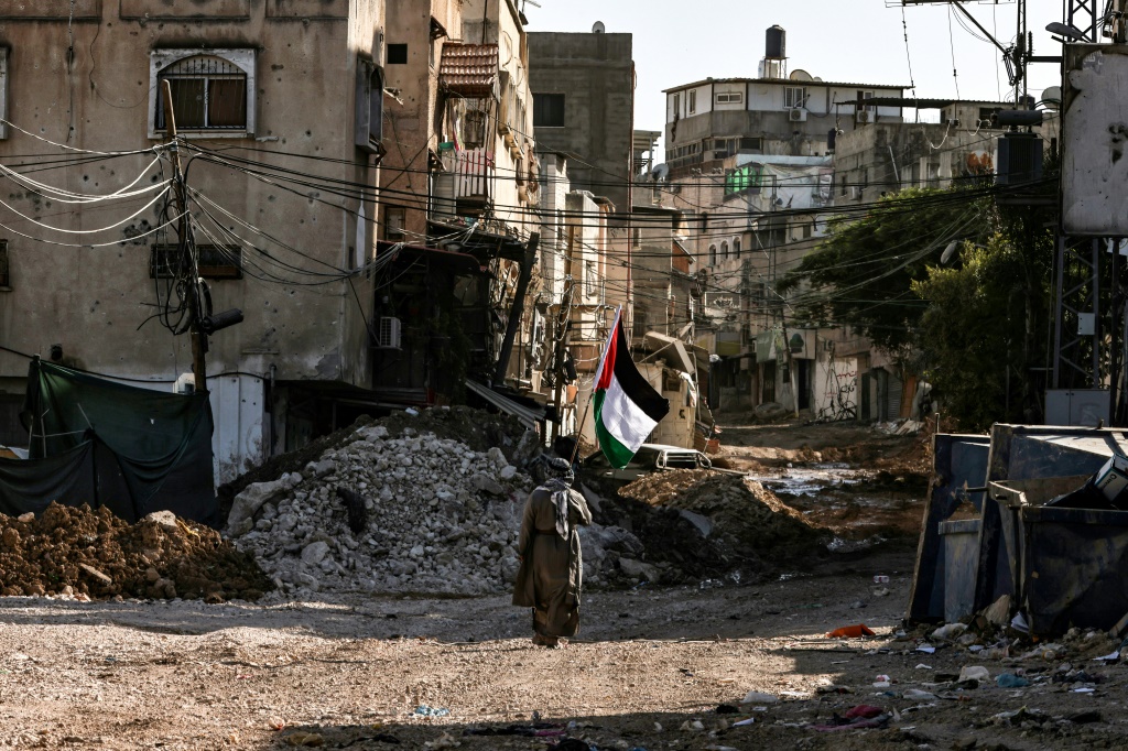 فلسطيني يرفع العلم الوطني أثناء وقوفه وسط الدمار الذي أعقب مداهمة جيش الاحتلال الإسرائيلي لمدينة طولكرم شمال الضفة الغربية المحتلة في 12 أيلول/سبتمبر 2024 (أ ف ب)   