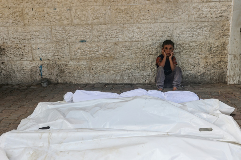 طفل يجلس بجوار جثث ضحايا القصف الإسرائيلي الذي استهدف مستشفى شهداء الأقصى في دير البلح وسط قطاع غزة (أ ف ب)