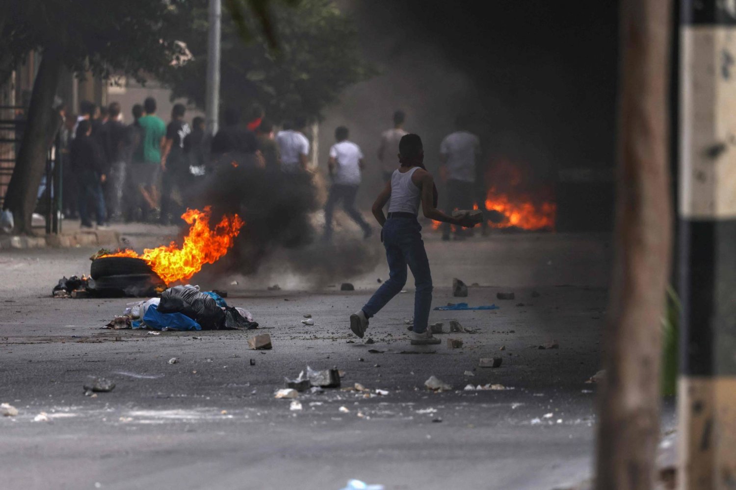 فلسطينيون يغلقون الطريق بالإطارات المشتعلة ويلقون الحجارة على القوات الإسرائيلية في مخيم بلاطة للاجئين شرق نابلس بالضفة الغربية (أ.ف.ب)