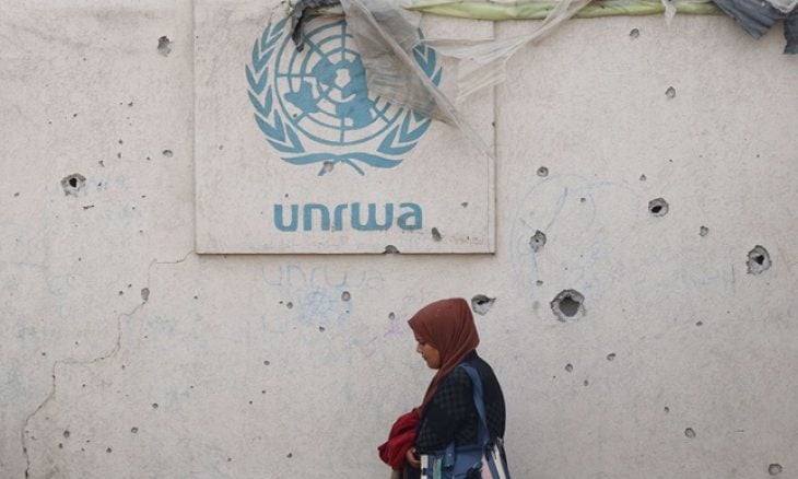 فلسطينية أمام جدار متضرر يحمل شعار الأونروا في مخيم للنازحين في رفح جنوب قطاع غزة في 28 مايو 2024(ا ف ب)