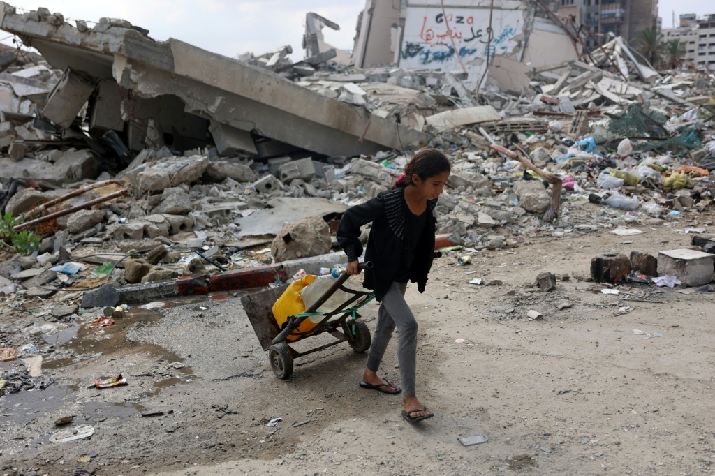 طفلة فلسطينية تجر صفائح مياه نظيفة تمر بمحاذاة أبنية مدمرة في مدينة غزة في شمال قطاع غزة في الثاني من تشرين الثاني /نوفمبر 2024 (أ ف ب)   